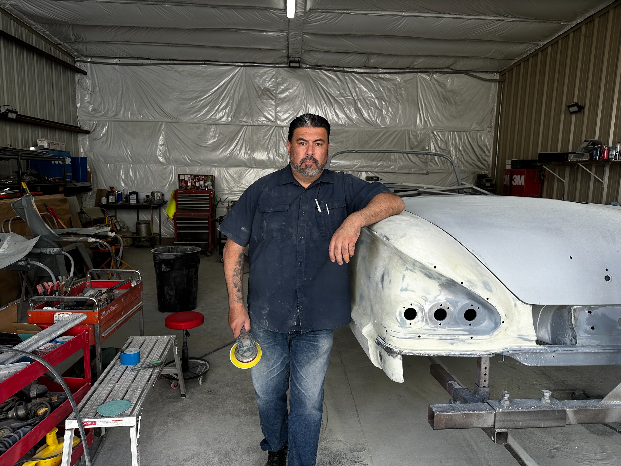 Anthony Cordova standing beside the 1958 Impala restoration in his shop